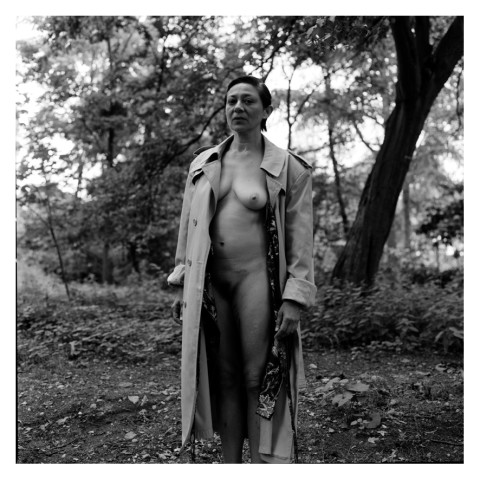Jeune femme portant un imperméable ouvert, au bois. Photographie en noir et blanc